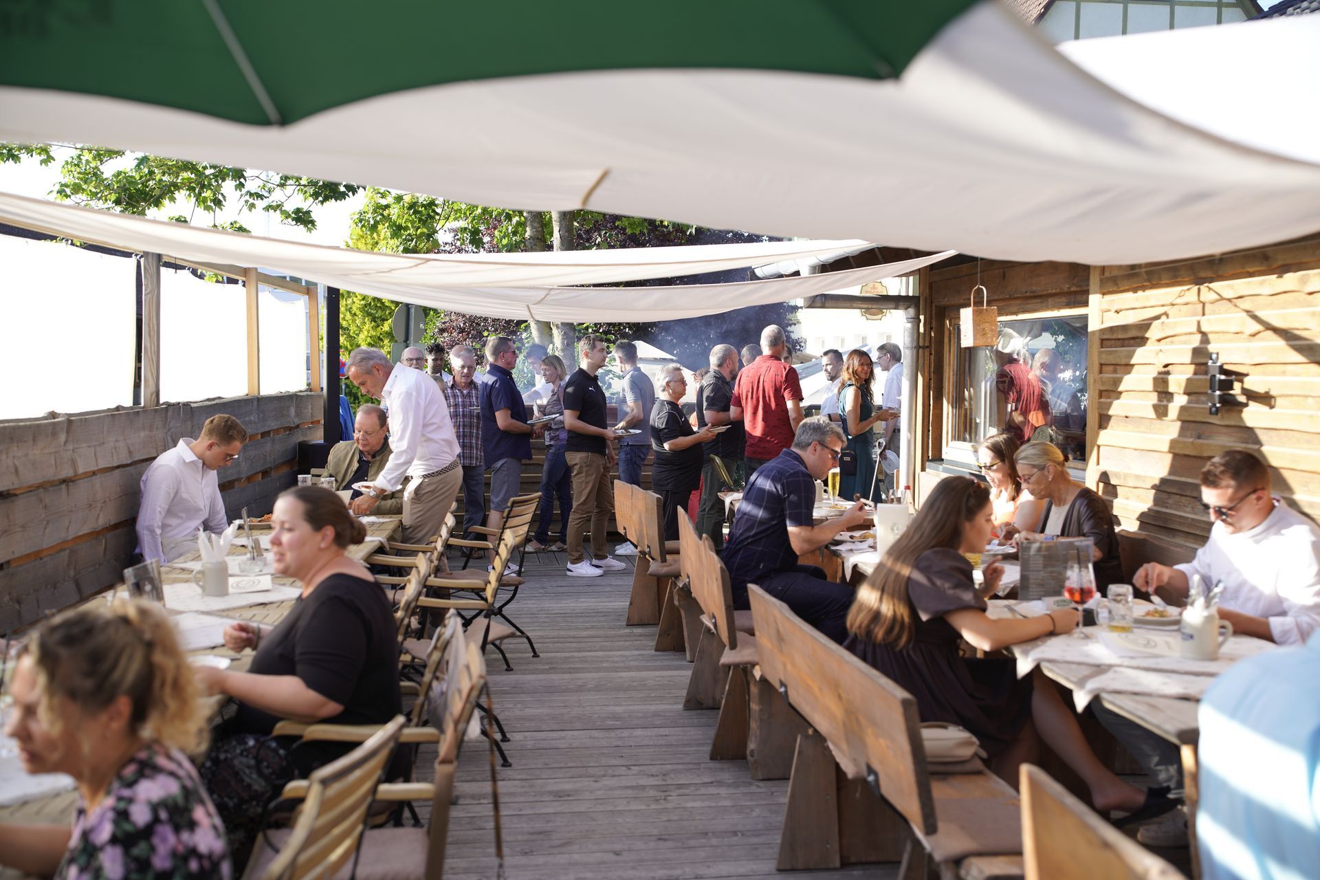 Gäste sitzen im Außenbereich unter Sonnenschirmen bei Feier