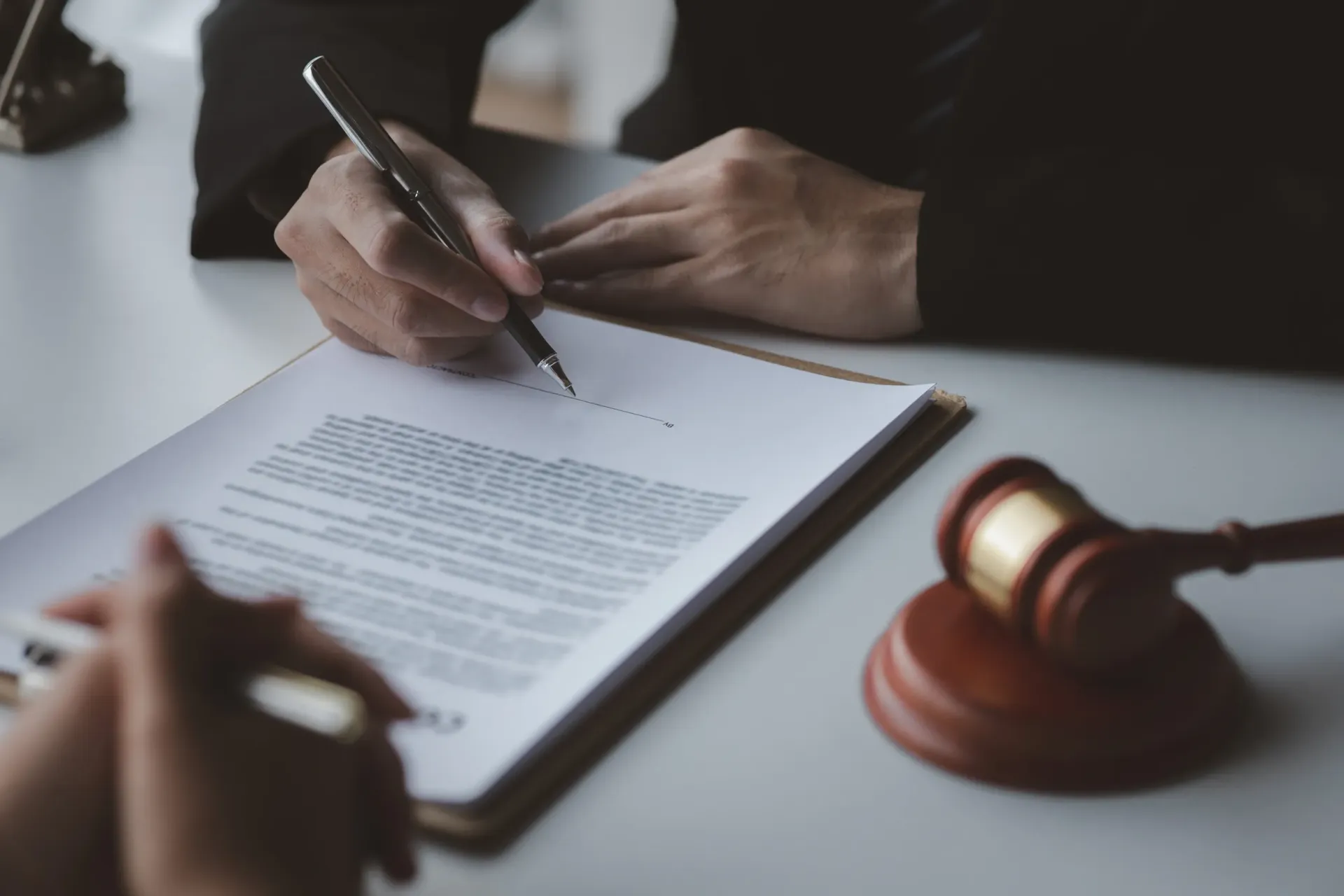 Persona firmando un documento legal en un escritorio, con el mazo en primer plano.