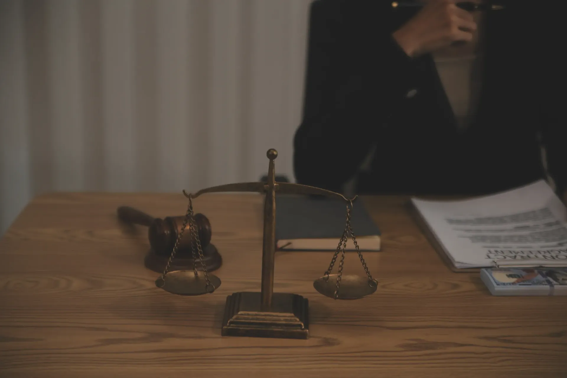 Balanza de la justicia, mazo, documentos y persona con traje sobre un escritorio de madera.