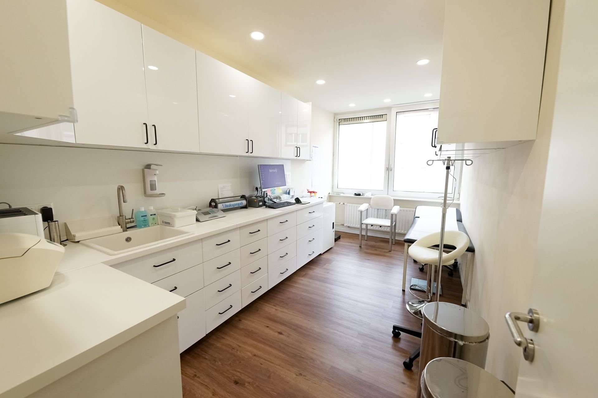 Eine Behandlungszimmer mit weißen Schränken, Holzböden und einer Spüle.