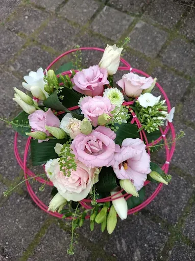 Composition florale dans un récipient gris texturé ; fleurs rose, violet et crème avec des brindilles et de la verdure.