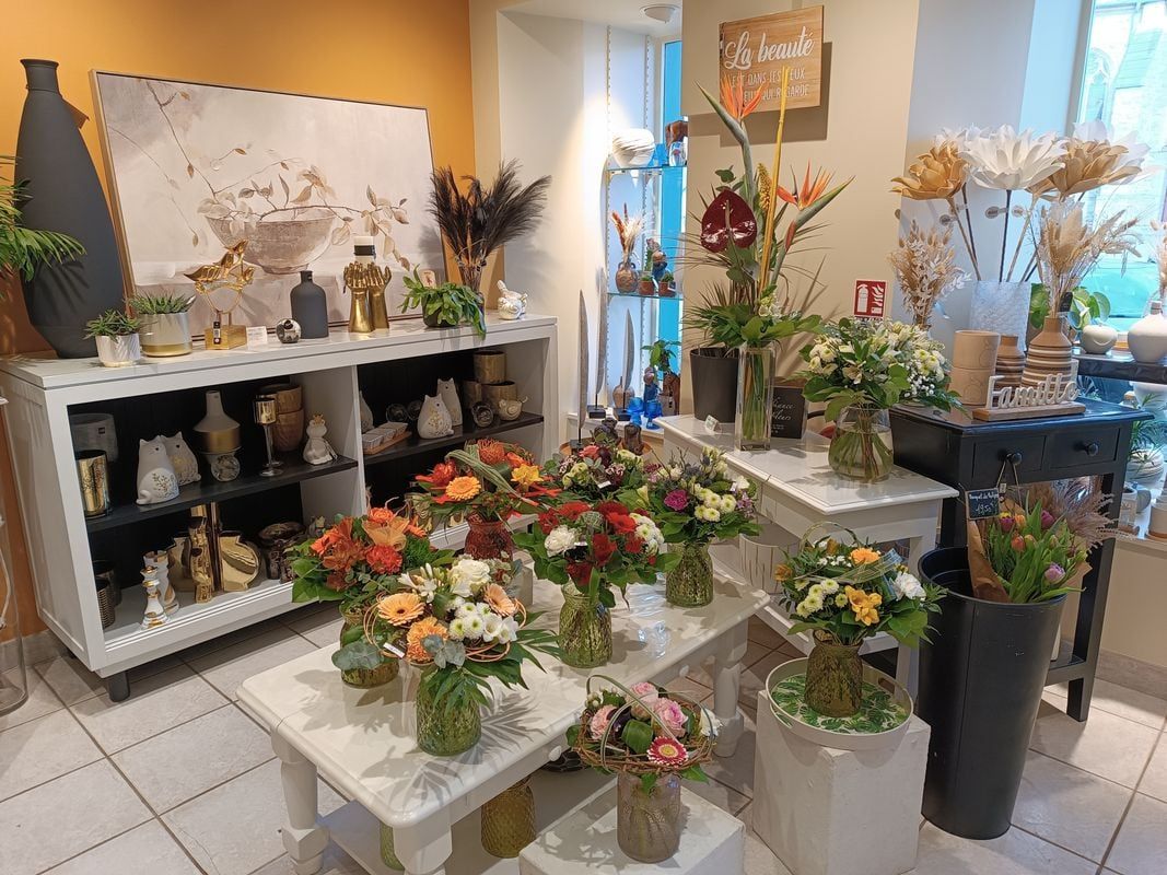Intérieur d'une boutique de fleurs avec des bouquets présentés sur des tables et des étagères blanches.