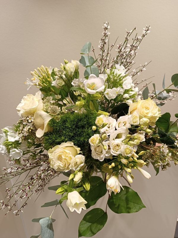Bouquet de fleurs blanc et vert composé de roses, d'eucalyptus et d'autres fleurs.