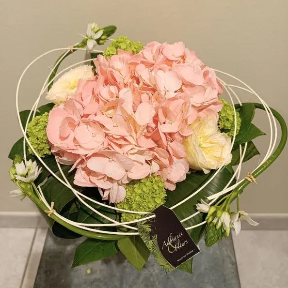 Des roses jaunes, des fleurs orange et de la gypsophile blanche dans un vase recouvert de toile de jute.
