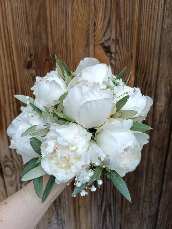 Bouquet de pivoines blanches et de verdures sur fond de bois brun.