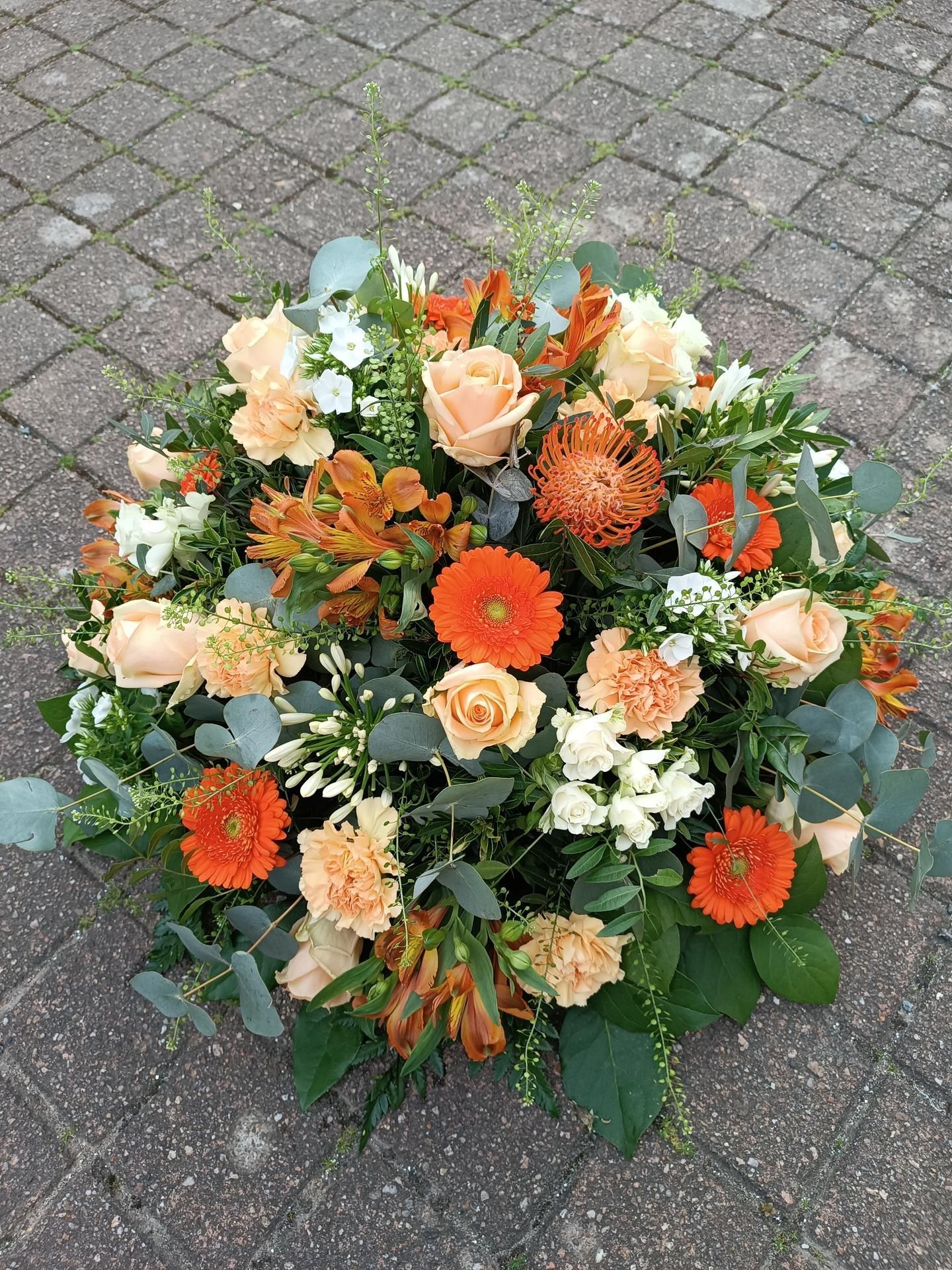 Composition florale ronde avec des fleurs orange et pêche sur une surface en briques.