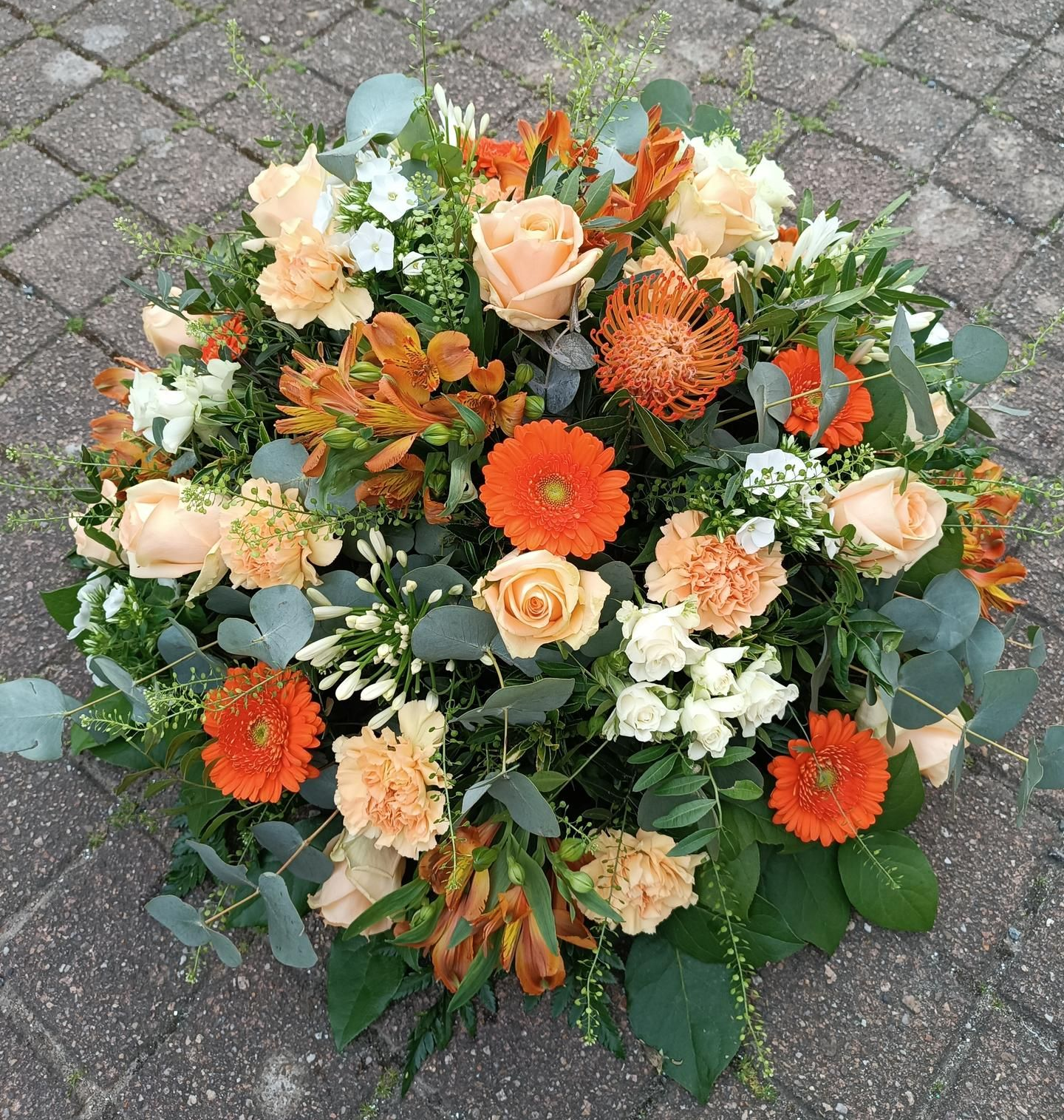 Composition florale de fleurs orange, pêche et blanc, avec de la verdure, sur une surface en pierre.