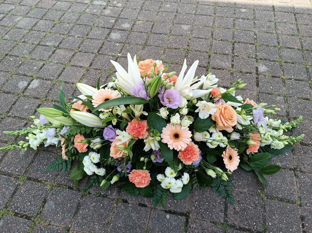 Composition florale avec des fleurs orange, pêche, blanc et violet sur une surface en pierre grise.