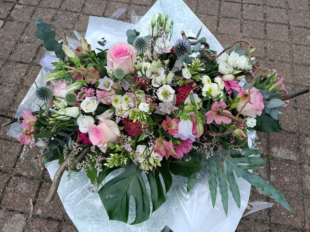 Gros plan sur une composition florale avec des roses roses, des fleurs blanc et rouge et du feuillage vert, enveloppée dans du papier blanc.