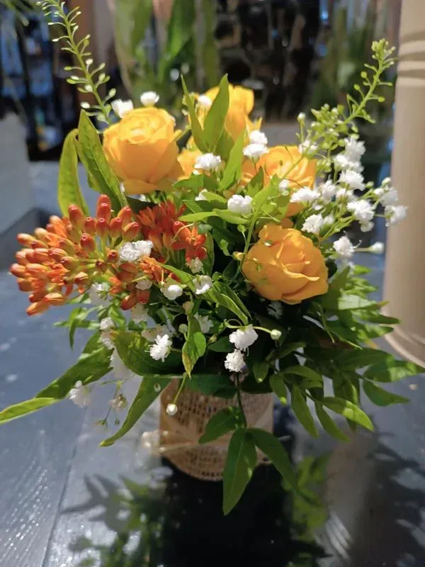Composition florale avec des roses jaunes, de la gypsophile blanche et des fleurs orange dans un bocal.