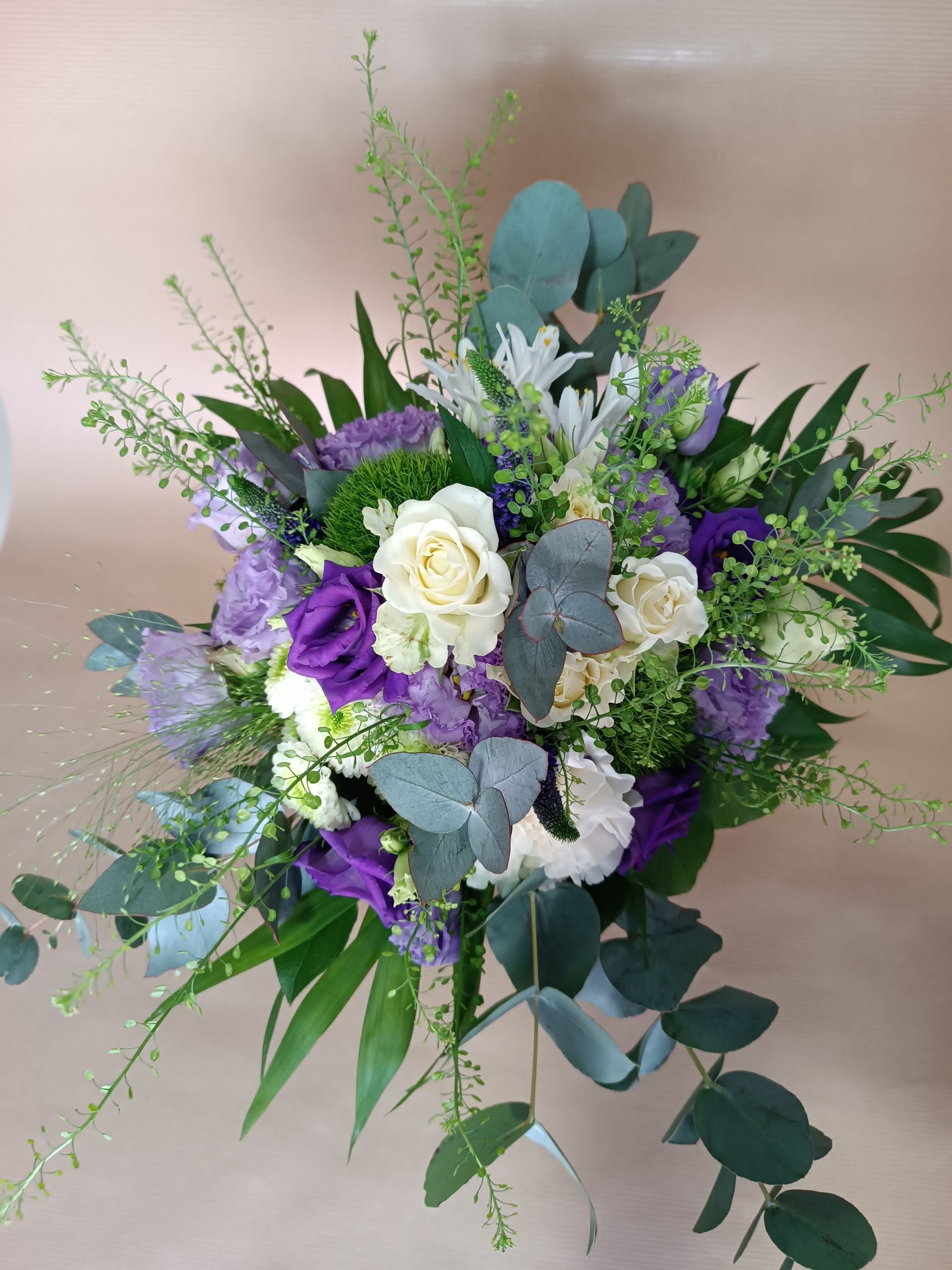 Bouquet de fleurs blanc, violet et vert avec de l'eucalyptus, sur un fond brun clair.