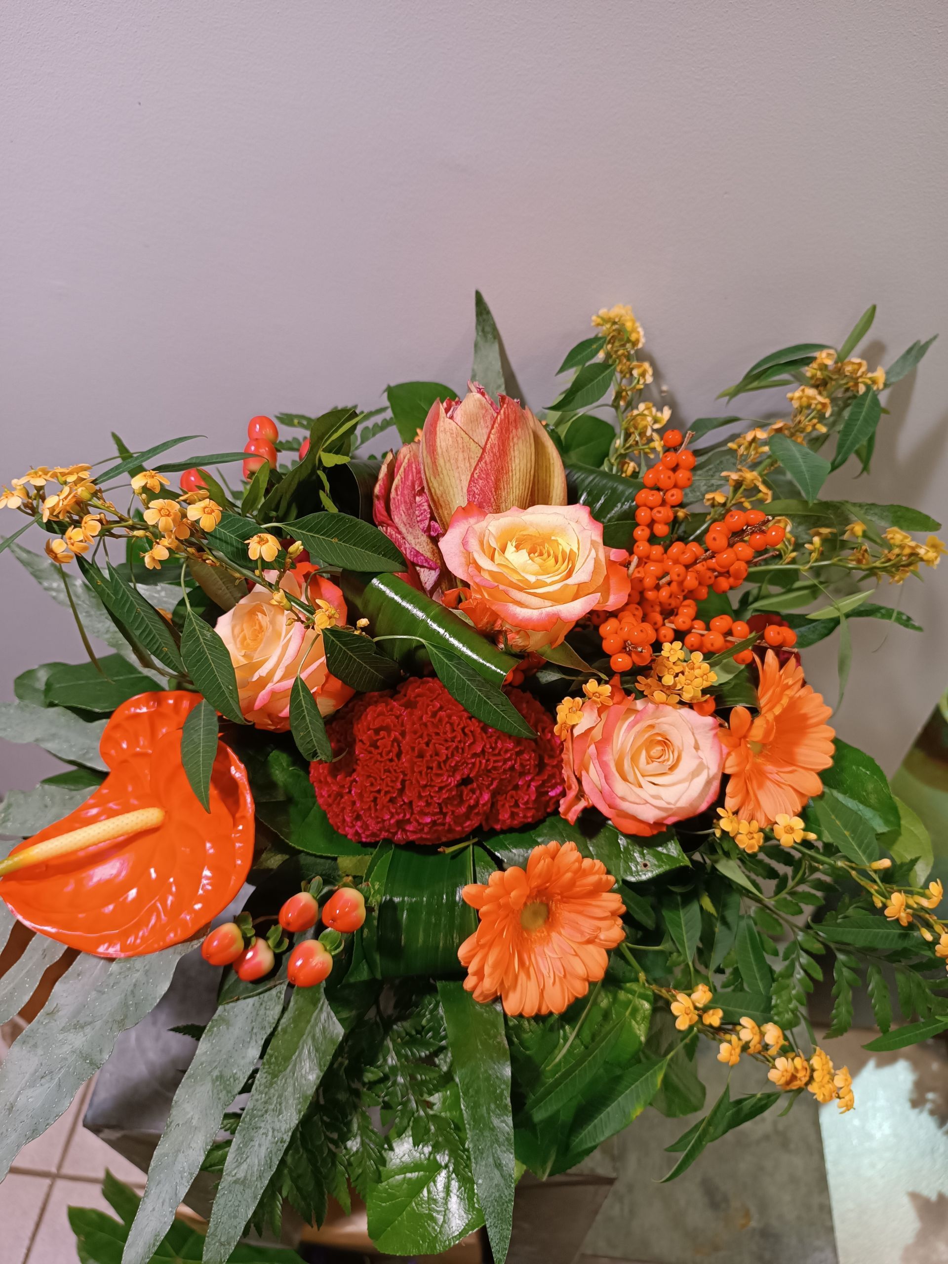 Bouquet de roses orange, d'anthuriums et d'autres fleurs avec de la verdure.