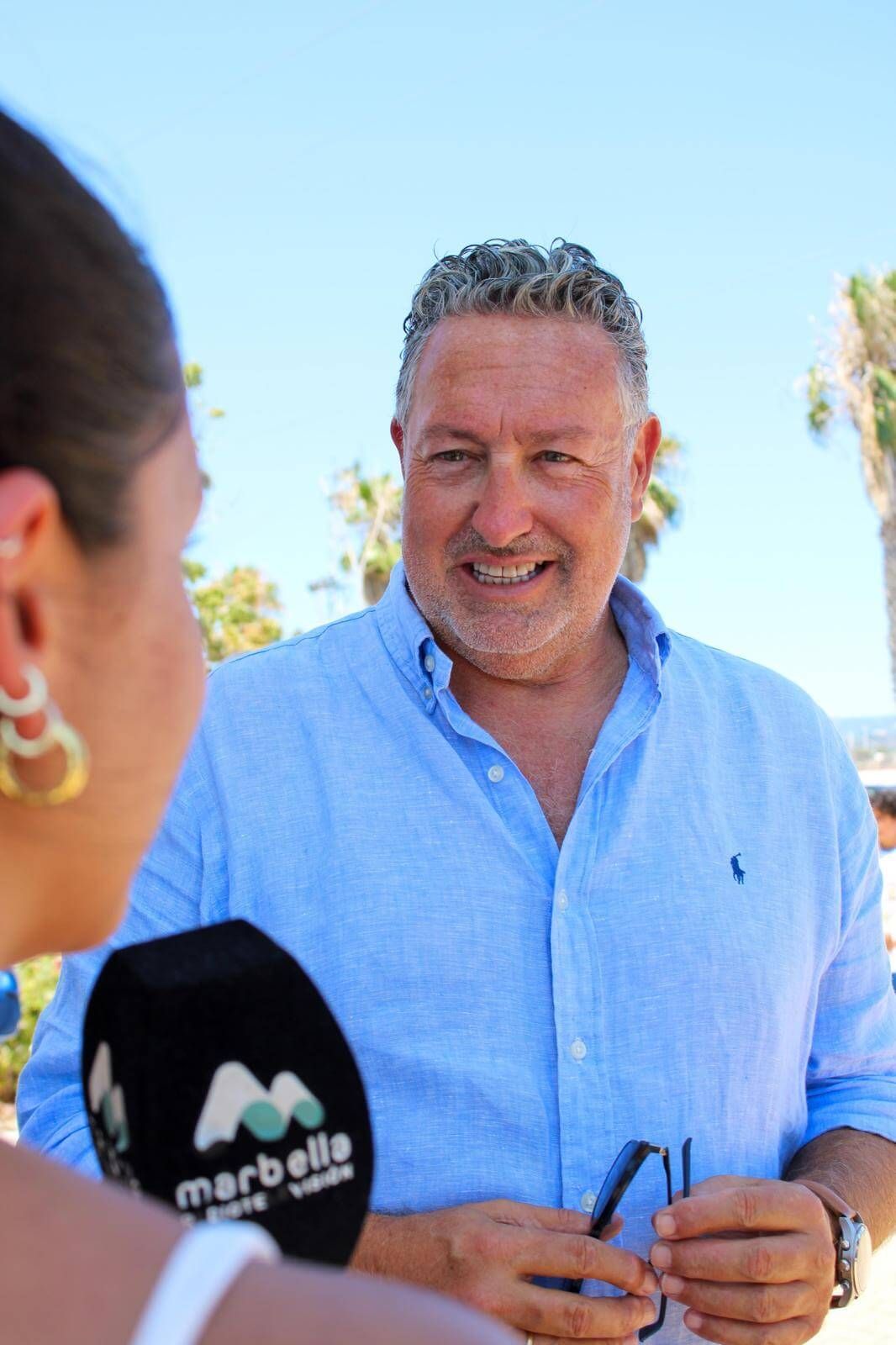 Un hombre con camisa azul habla con una mujer frente a un micrófono de Marbella.