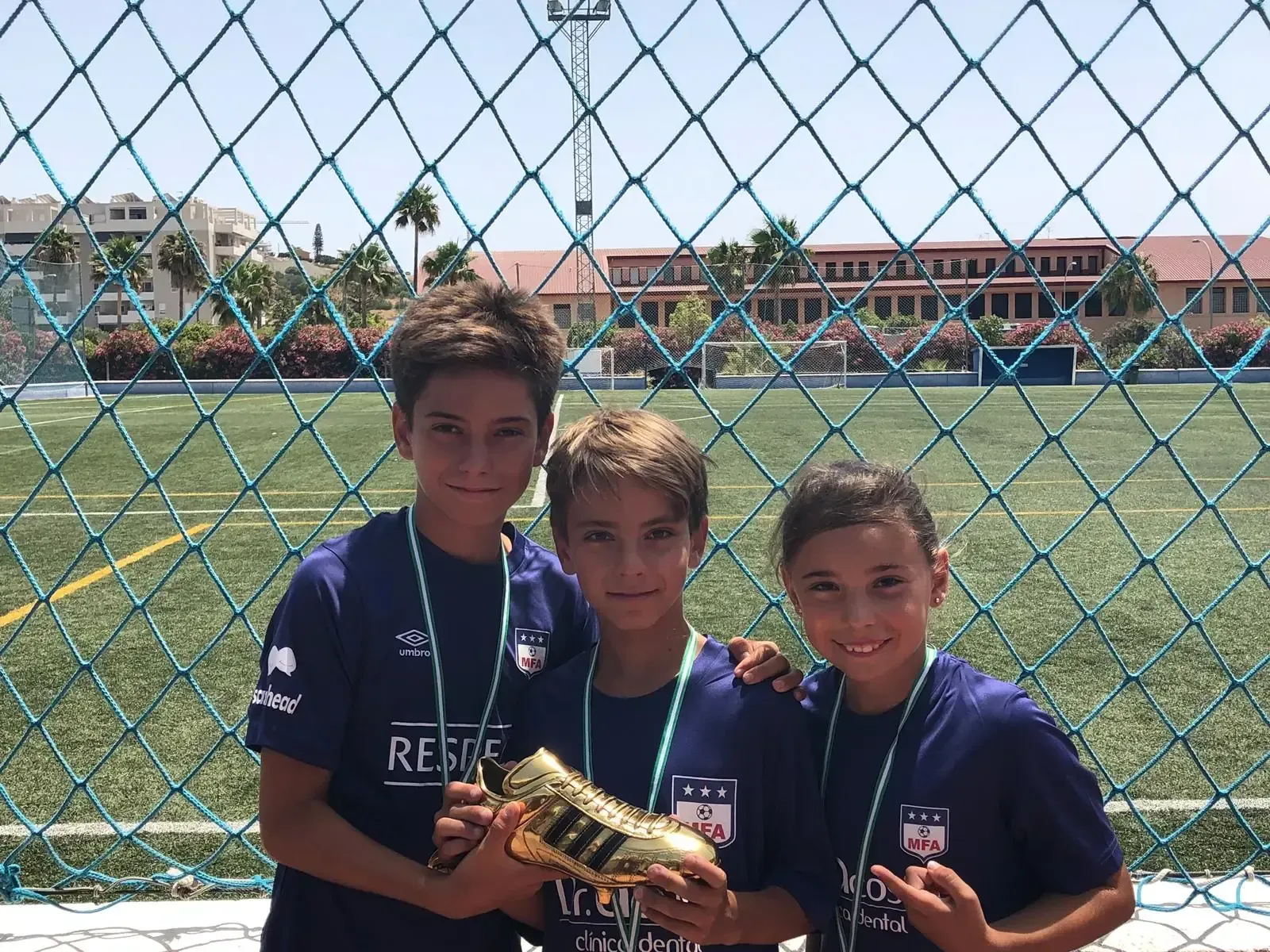 Tres jóvenes posan para una foto frente a una valla de alambre.
