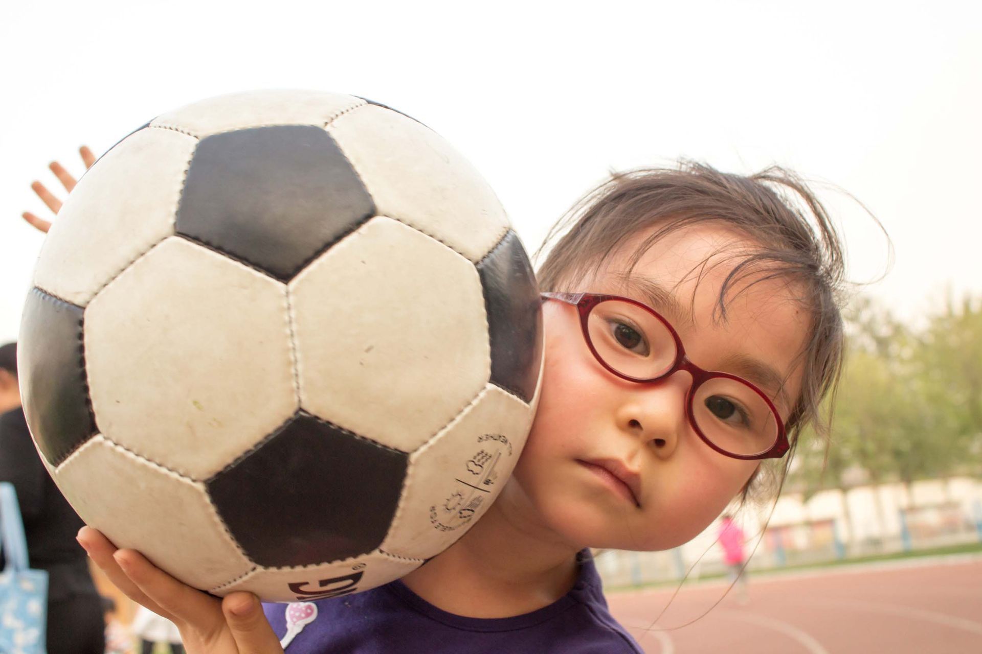 Una niña que lleva gafas sostiene un balón de fútbol.