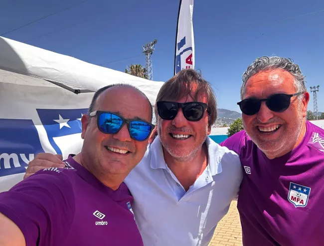 Tres hombres con gafas de sol y camisetas moradas posan para una fotografía.