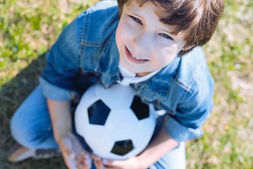 Un niño pequeño está sentado en el césped sosteniendo un balón de fútbol.