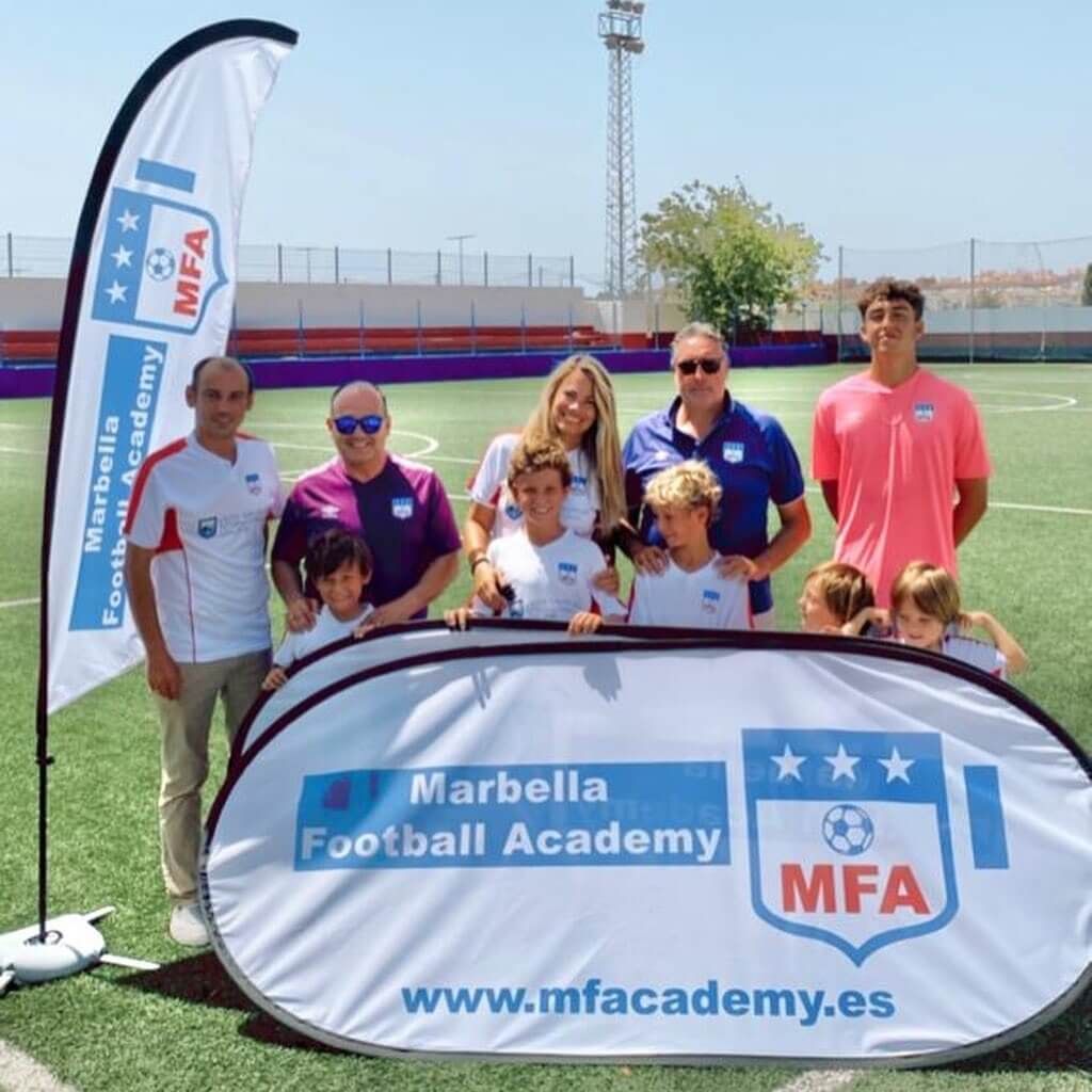 Un grupo de personas de pie frente a una pancarta de la academia de fútbol de Marbella.