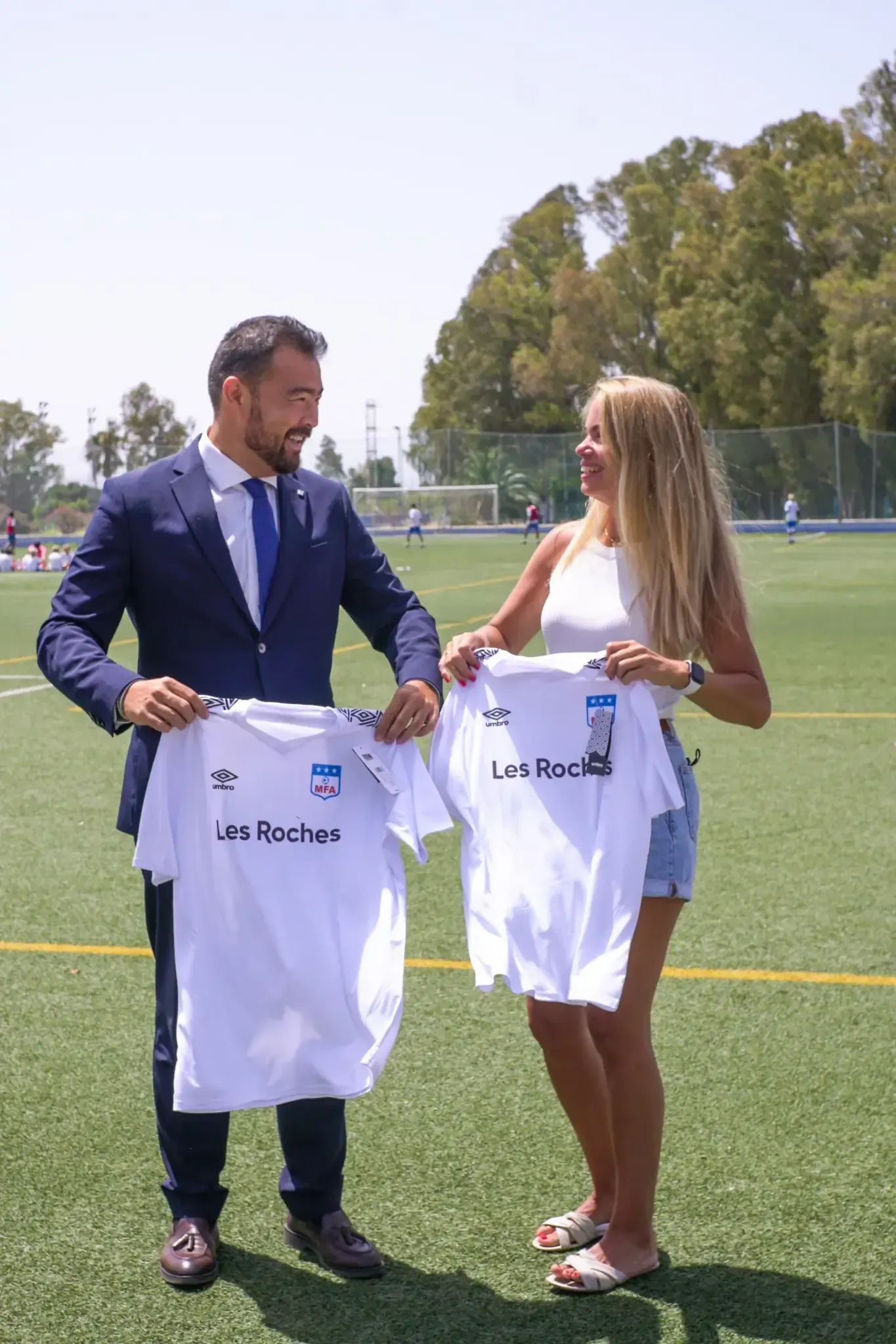 Un hombre y una mujer sostienen camisetas en un campo de fútbol.