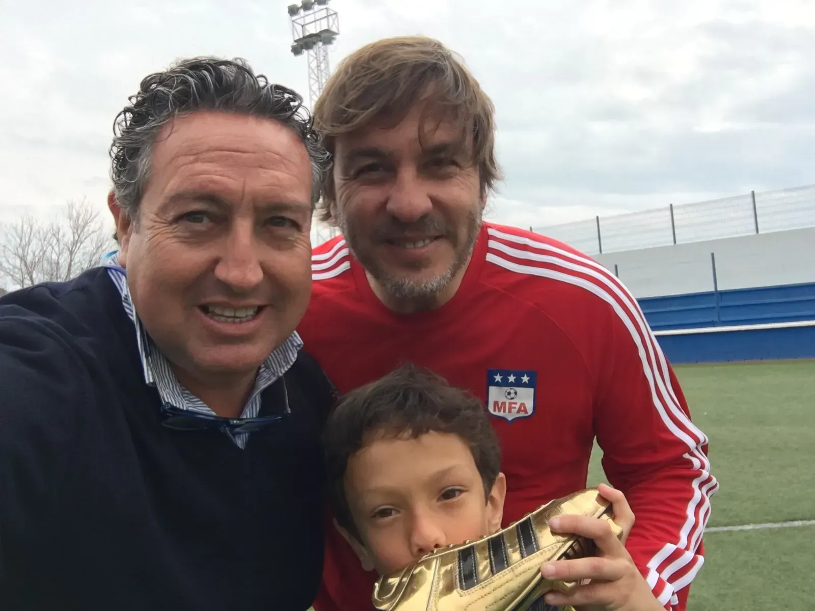 Tres hombres posan para una foto con un niño pequeño que sostiene un trofeo.