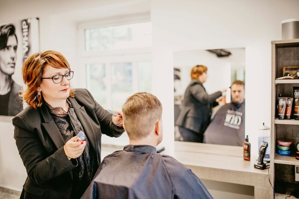 Eine Frau schneidet die Haare eines Mannes in einem Friseursalon