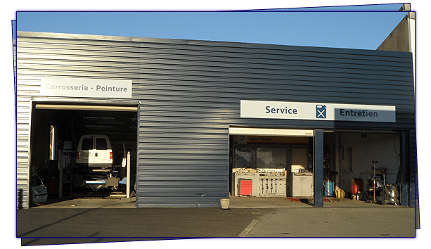 Extérieur du garage avec des travées ouvertes ; un véhicule sur un pont élévateur à l'intérieur de l'une, un bureau visible dans une autre.