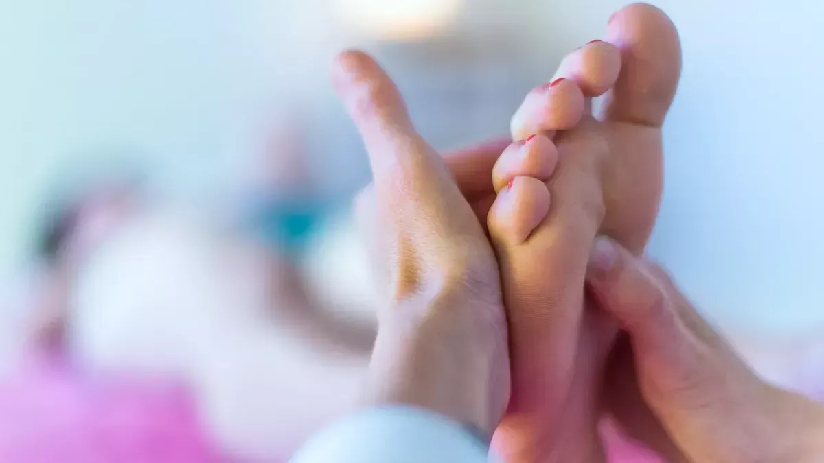 Gros plan sur des mains tenant délicatement les pieds d'une personne sur un fond flou et doux.