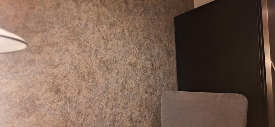 Dunkle Zimmerecke mit strukturierter Tapete, Stehlampenkante, Stuhllehne und dunklem Schrank