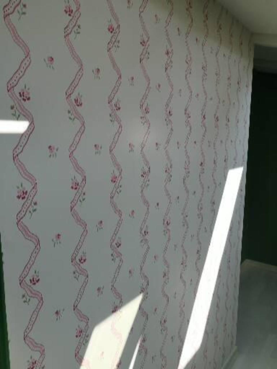 Weisse Wand mit rosa gewellter Tapete in einem von Sonnenlicht und Schatten erhellten Raum.
