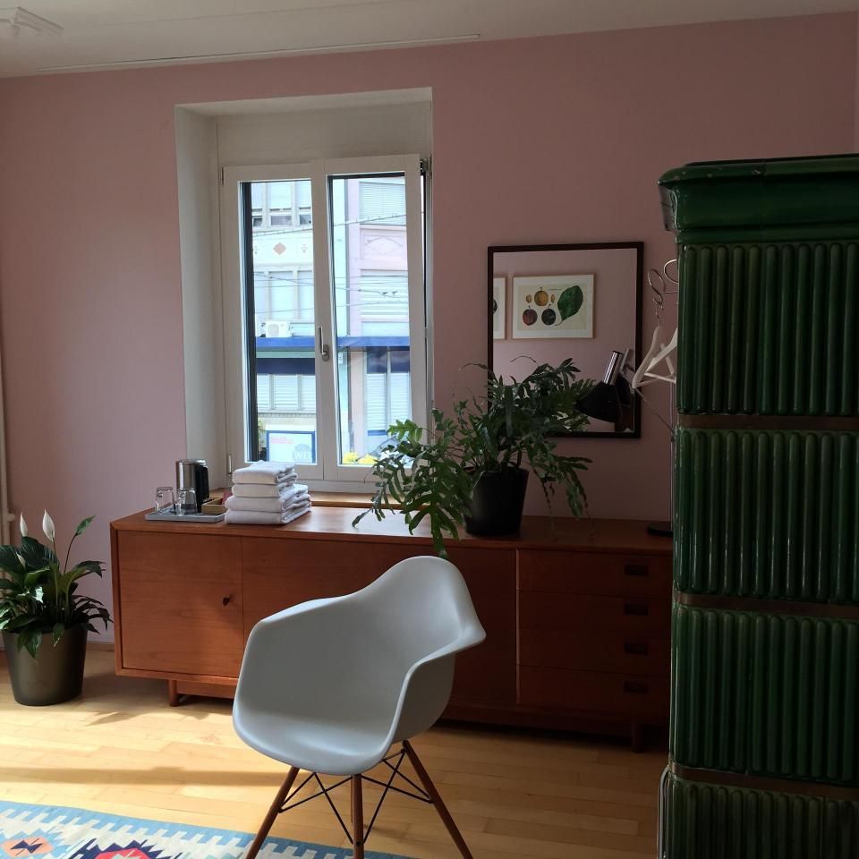Rosa Zimmer mit weissem Stuhl, hölzernem Sideboard, Pflanzen und Sonnenlicht durch ein Fenster