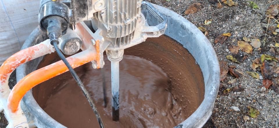 Orangefarbene Bohrmaschine vermischt braunen Schlamm in einem Metalleimer im Freien