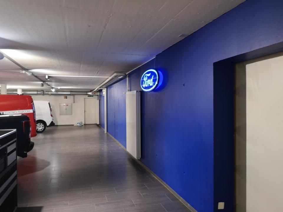 Parkhaus mit blauer Wand, Leuchtreklame und geparkten Fahrzeugen auf der linken Seite.