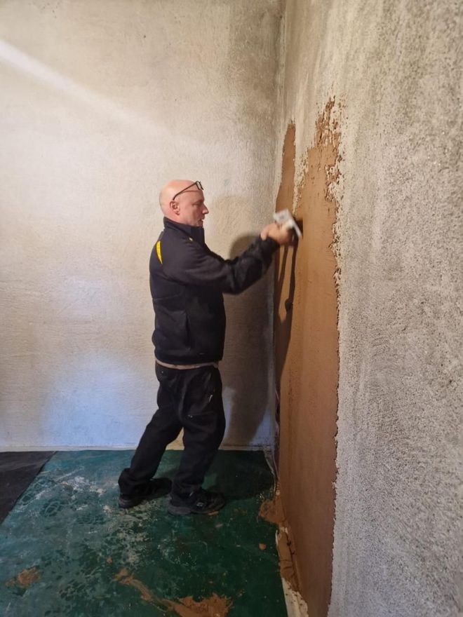 Person, die mit einer Kelle Gips an eine Wand in einem Zimmer streicht