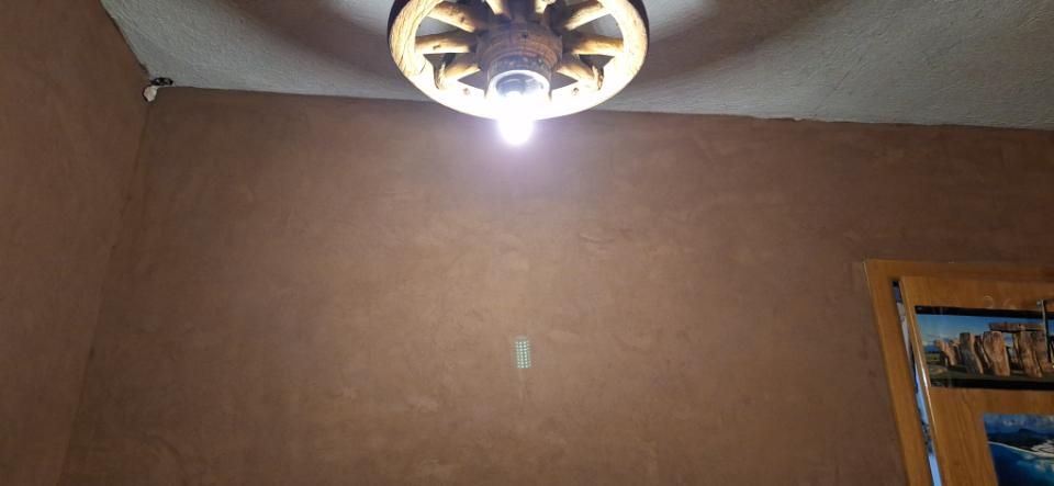 Eine Deckenleuchte wirft helles Licht auf eine braune Wand, rechts ist der Rand eines gerahmten Bildes zu sehen.