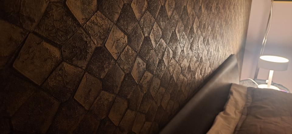 Strukturierte braune Wand neben einem Bett und einer Nachttischlampe in einem schwach beleuchteten Schlafzimmer