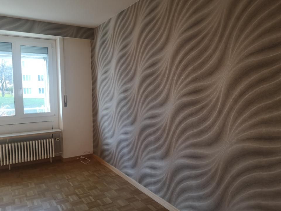 Leeres Zimmer mit gewellter beiger Tapete, einem Fenster, einem Heizkörper und gefliestem Boden.