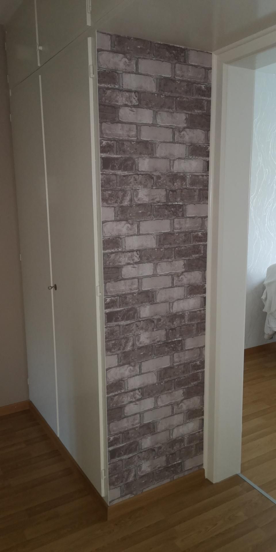 Schmale Akzentwand mit Ziegelmuster zwischen beigen Wänden in einem Flur mit Holzboden.