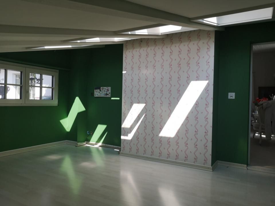 Leerer Raum mit grünen Wänden, einer weiß gemusterten Wand und Sonnenlicht, das durch die Fenster strömt.