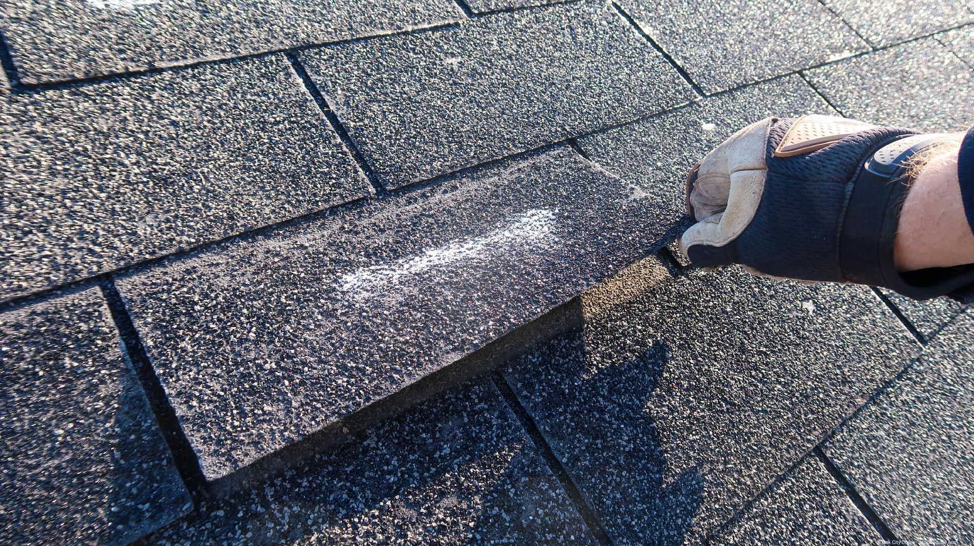 Hand trägt Material auf Asphalt­schindeln eines Hausdachs auf.