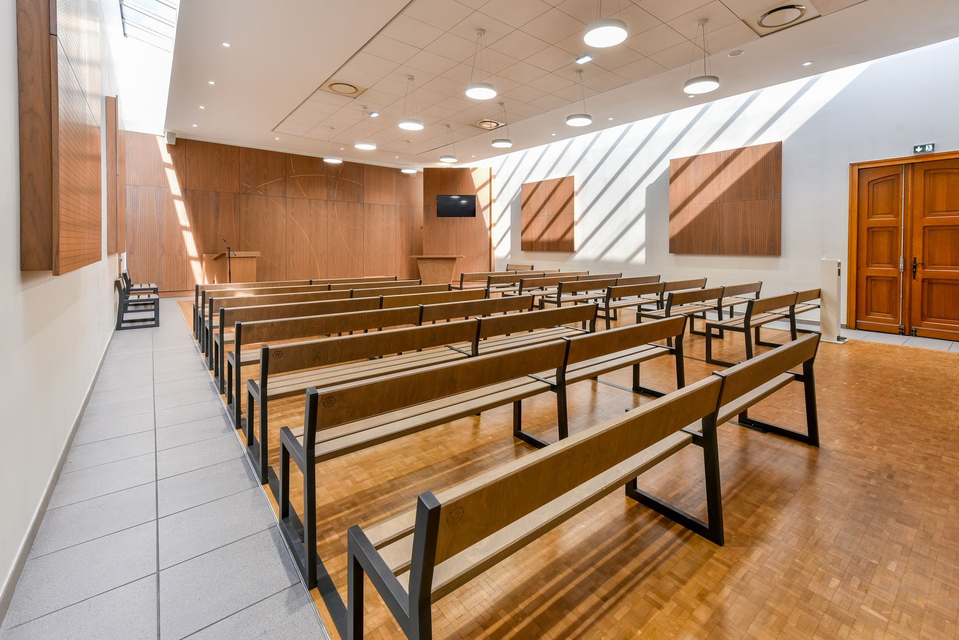 Salle d'audience vide avec bancs en bois, banc des juges et fenêtres lumineuses grâce à un puits de lumière