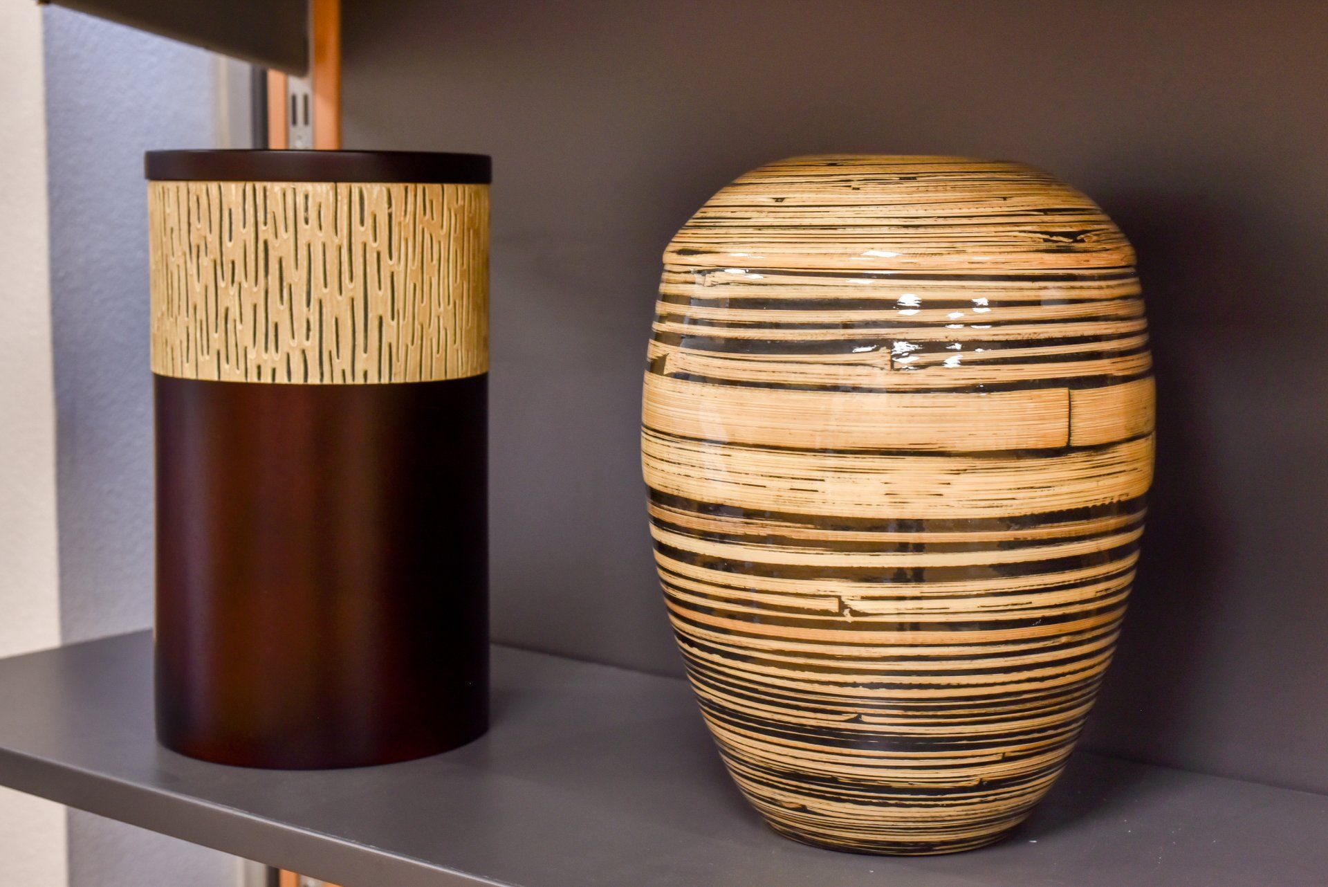 Deux vases décoratifs sur une étagère, l'un brun foncé avec une bande beige et l'autre beige avec des rayures foncées.