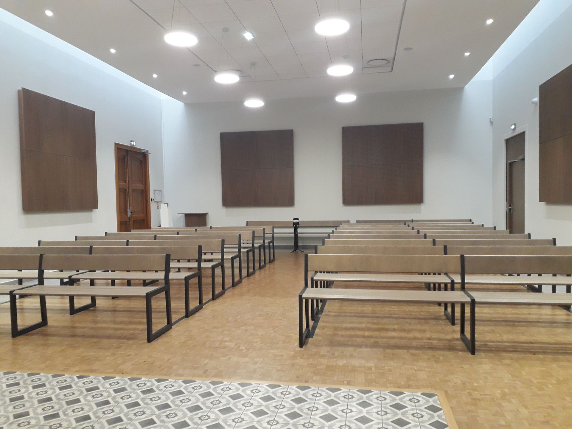 Salle d'audience vide avec bancs, pupitre des témoins et murs lambrissés sous une lumière vive au plafond