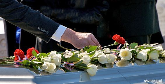 Une personne dépose des roses blanches et rouges sur un cercueil lors d'une cérémonie funéraire