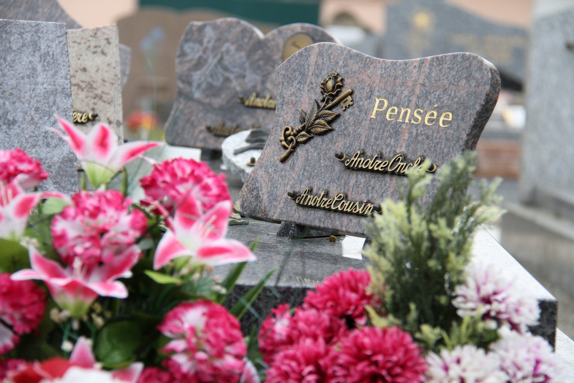 Des fleurs sur une pierre tombale dans un cimetière, avec une plaque commémorative grise portant l'inscription Pensée.