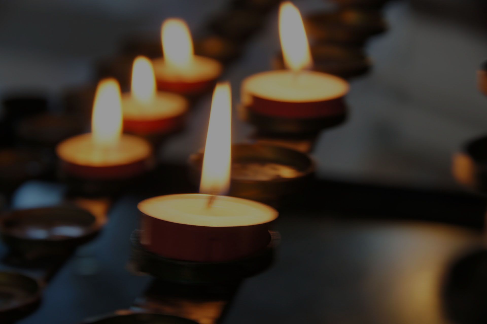 Des bougies chauffe-plat allumées brillent sur une surface sombre, avec plusieurs flammes floues en arrière-plan.