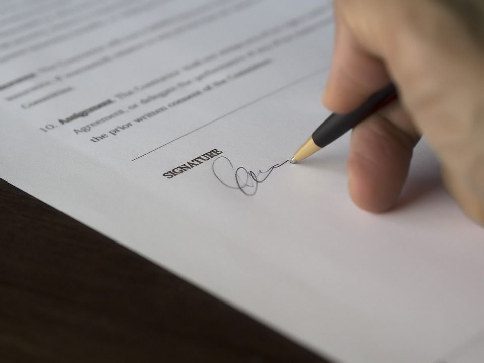 Signature manuscrite d'un document au stylo noir sur un bureau