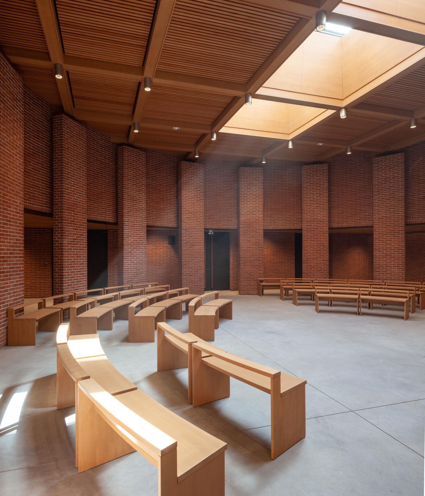 Bancs en bois courbés dans une chapelle ou un hall moderne aux murs de briques et au plafond en bois clair