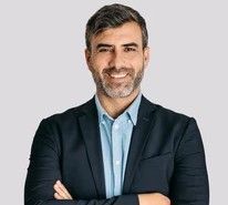 Un hombre con traje y camisa azul sonríe con los brazos cruzados.