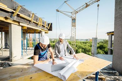 Zwei Bauarbeiter betrachten Baupläne auf einer Baustelle.