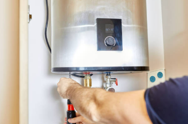 Une personne travaille sur un chauffe-eau à l'aide d'un tournevis. Le chauffe-eau est en métal.